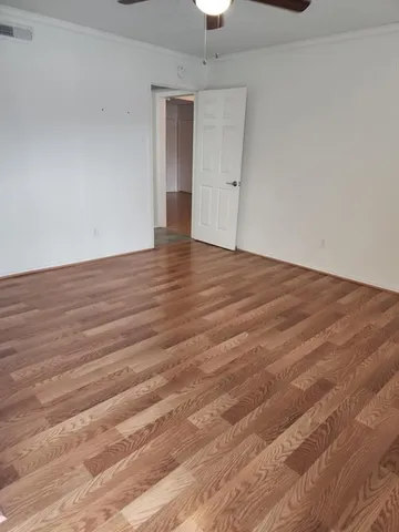 a view of an empty room with wooden floor and a ceiling fan