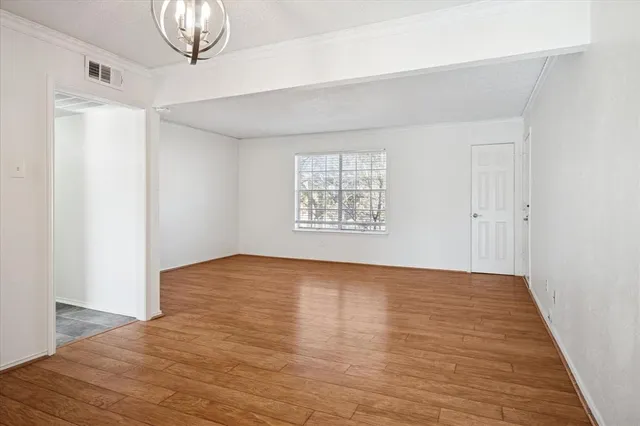 an empty room with wooden floor chandelier and windows