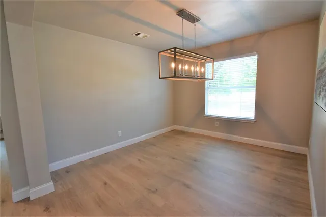an empty room with wooden floor chandelier and windows