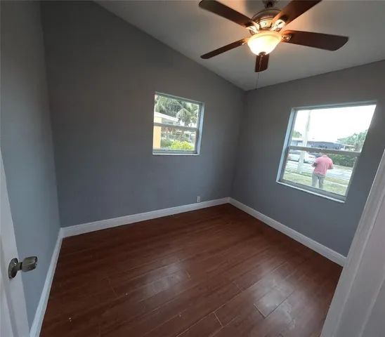an empty room with wooden floor fan and windows