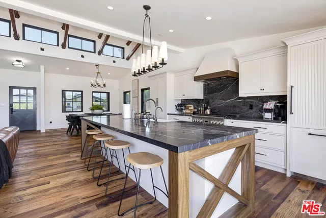 an open kitchen with granite countertop a stove a sink a dining table and chairs with wooden floor