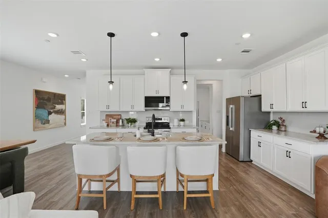 a kitchen with stainless steel appliances kitchen island granite countertop a dining table chairs refrigerator and microwave