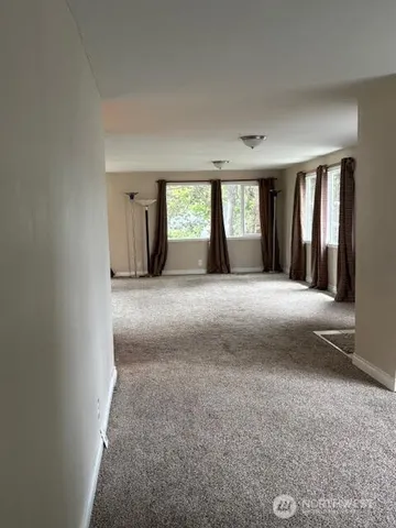 a view of an empty room with window and a kitchen