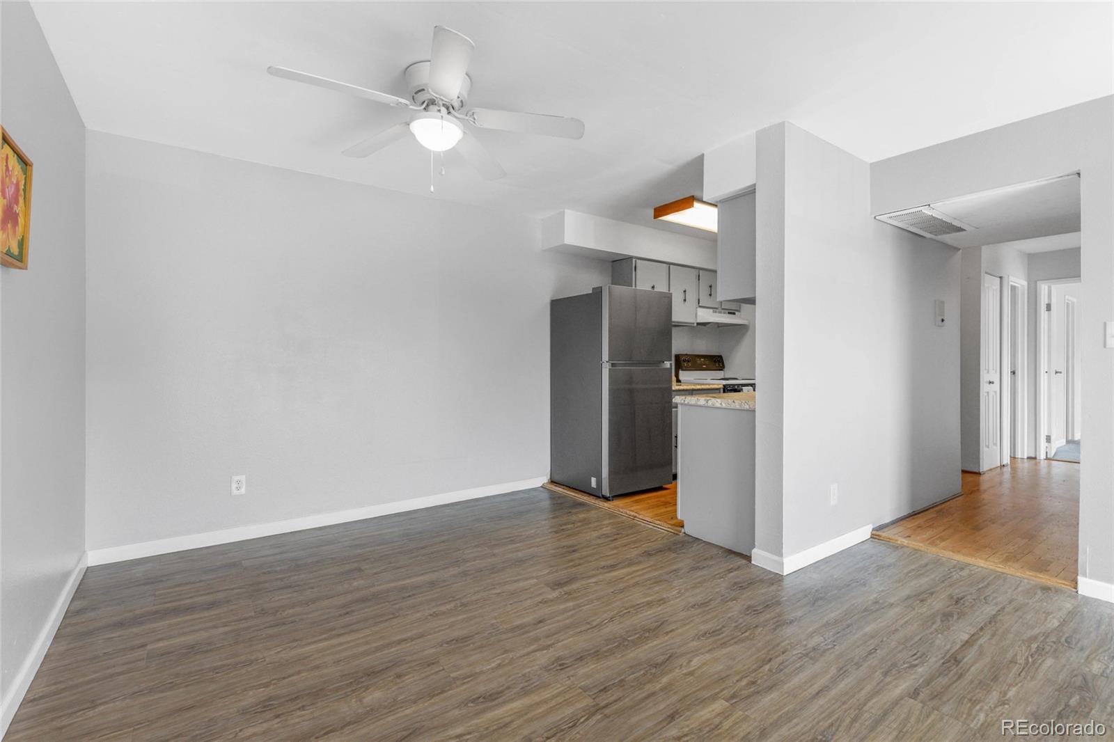 7755 East Quincy Avenue, Unit 205A5 Denver, CO 80237 - Photo 9 of 23 an empty room with wooden floor ceiling fan and kitchen view
