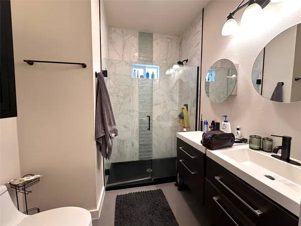 a bathroom with a double vanity sink a toilet a mirror and shower