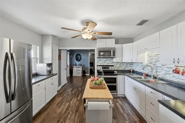 a kitchen with stainless steel appliances a stove a sink dishwasher a refrigerator white cabinets and wooden floor