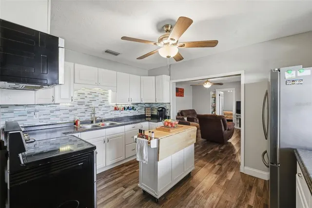 a kitchen with stainless steel appliances kitchen island granite countertop a sink dishwasher a stove top oven a refrigerator with island and cabinets
