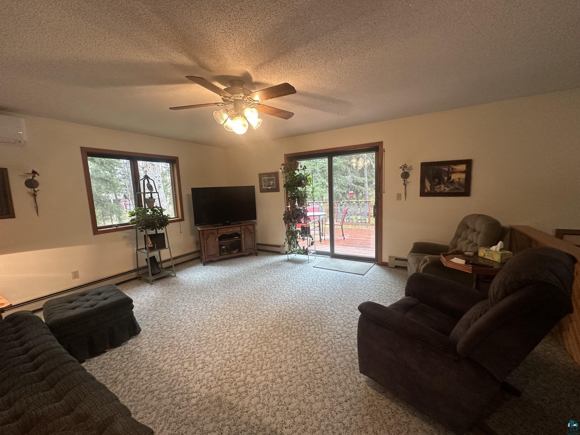 81 Hautaluoma Road Esko, MN 55733 - Photo 4 of 43 Spacious living area featuring patterned carpet flooring, a ceiling fan with integrated lighting, wood-trimmed windows, and a sliding glass door leading to an outdoor deck