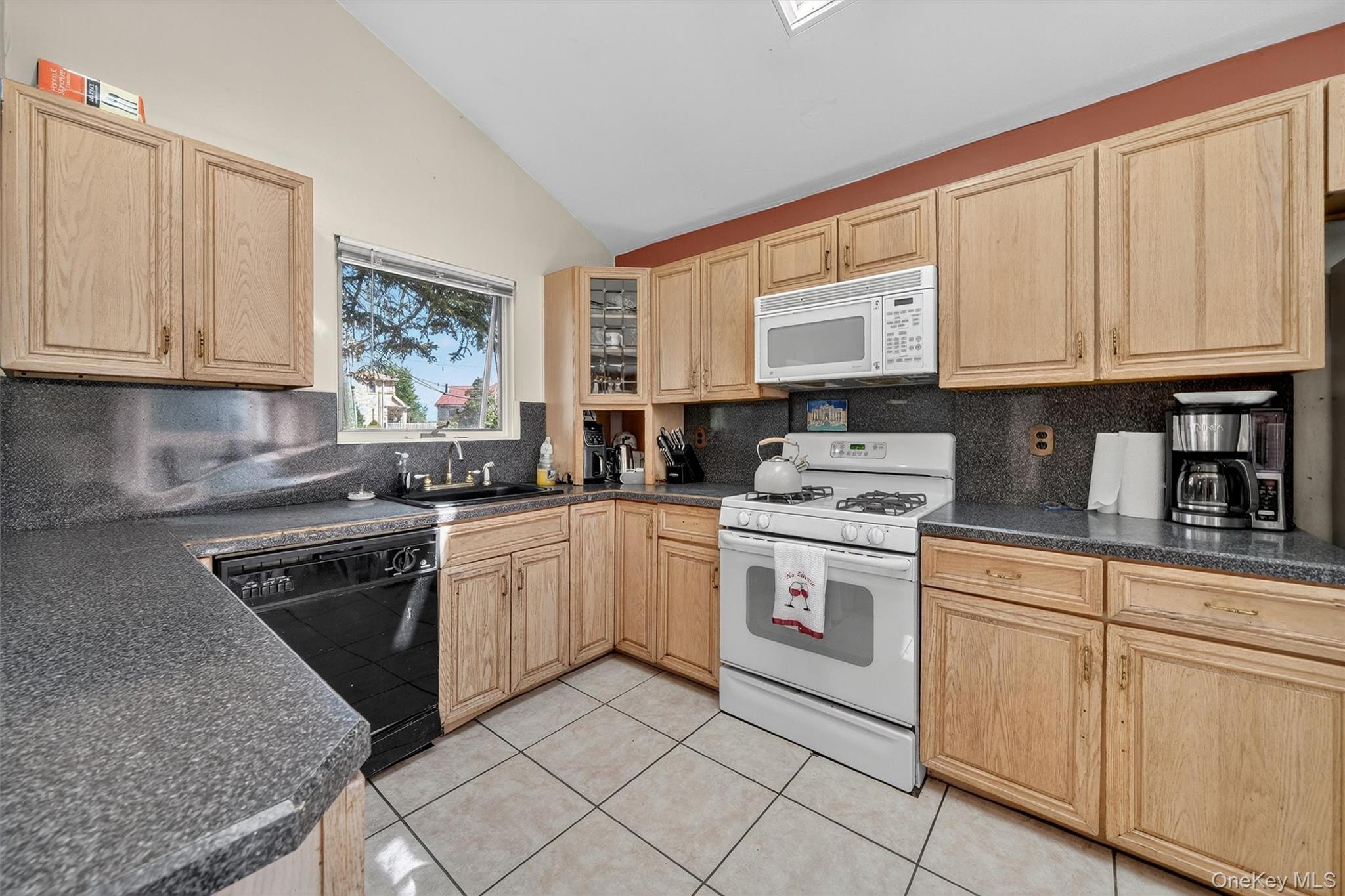 3384 Country Club Road Bronx, NY 10465 - Photo 13 of 48 Kitchen with light brown cabinetry, white appliances, vaulted ceiling, tasteful backsplash, and light tile patterned floors