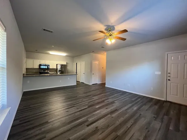 a view of an empty room with kitchen and window