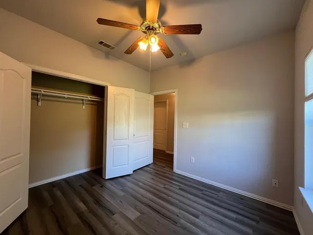 an empty room with wooden floor closet fan and windows