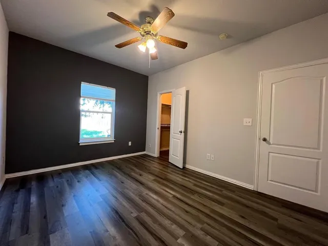 an empty room with wooden floor chandelier fan and windows