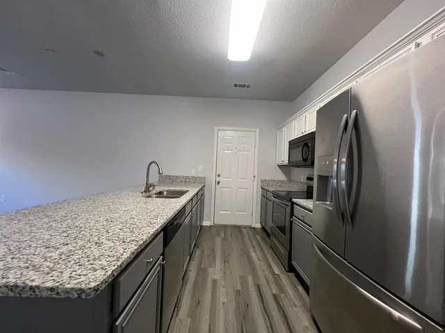 a kitchen with kitchen island granite countertop stainless steel appliances cabinets a sink and a refrigerator