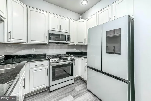 a kitchen with stainless steel appliances granite countertop white cabinets and a stove a refrigerator with white cabinets