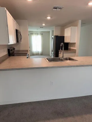 a large kitchen with kitchen island granite countertop a sink a stove a microwave a refrigerator and white cabinets