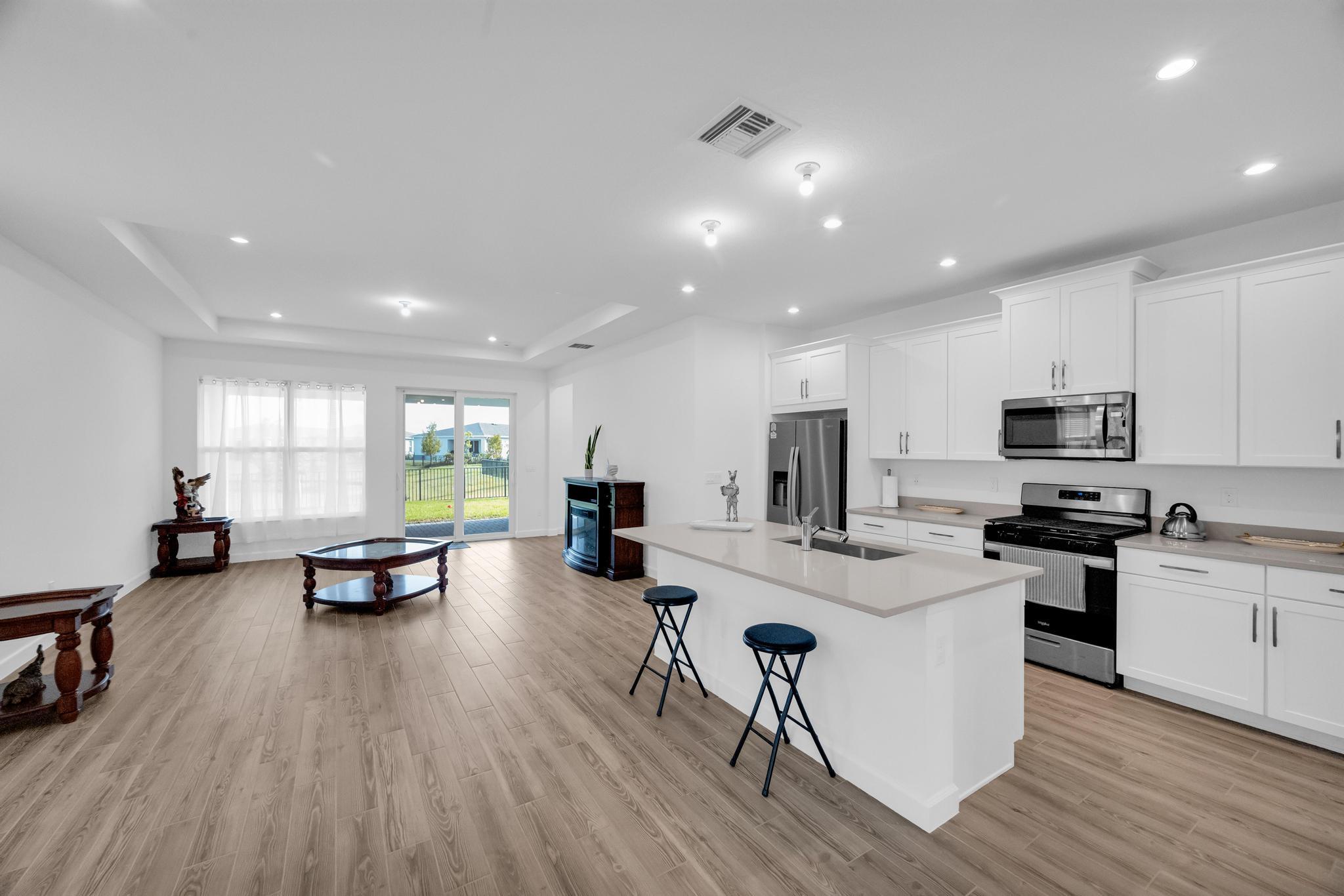 9060 Remy Lane Port St. Lucie, FL 34987 - Photo 8 of 33 a kitchen with stainless steel appliances kitchen island granite countertop a stove a sink a refrigerator and white cabinets with wooden floor