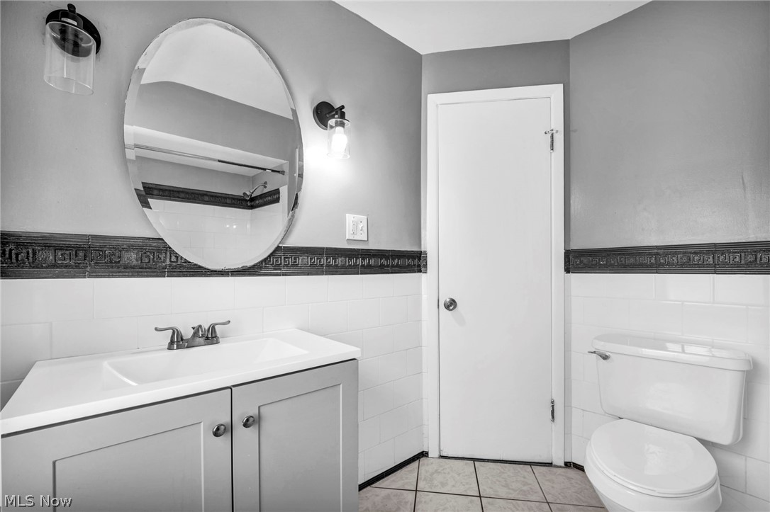 2313 North Taylor Road Cleveland Heights, OH 44112 - Photo 25 of 32 Bathroom featuring a single vanity with integrated sink, oval mirror, two sconce light fixtures, white subway tile wainscoting, and a toilet