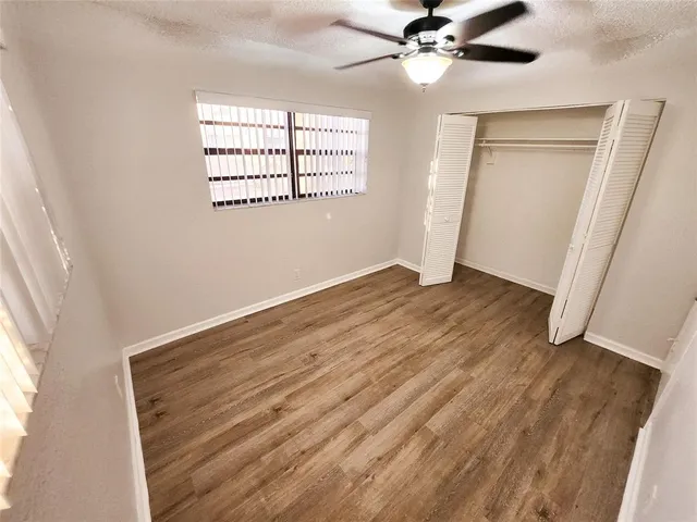 an empty room with wooden floor fan and windows