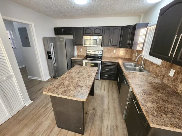 a kitchen with stainless steel appliances granite countertop wooden cabinets and a stove top oven with wooden floor