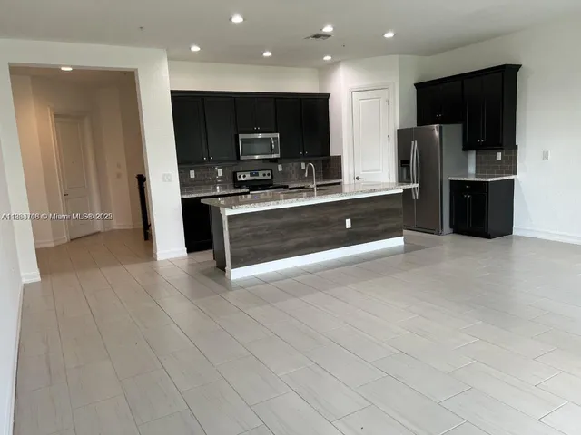 an open kitchen with stainless steel appliances kitchen island granite countertop a refrigerator a sink a stove and oven with wooden floor