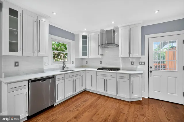 a kitchen with stainless steel appliances granite countertop a sink a stove a refrigerator and white cabinets with wooden floor