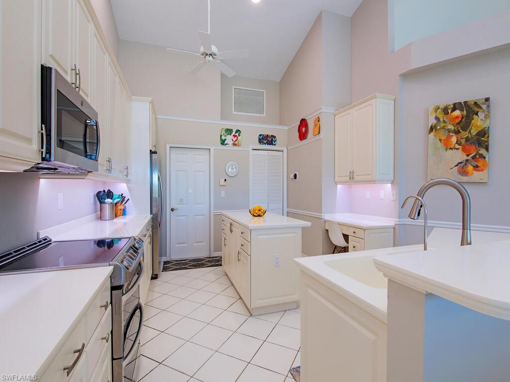 1832 Imperial Golf Course Boulevard Naples, FL 34110 - Photo 6 of 24 Kitchen featuring stainless steel appliances, a kitchen island, white cabinets, a high ceiling, and a ceiling fan