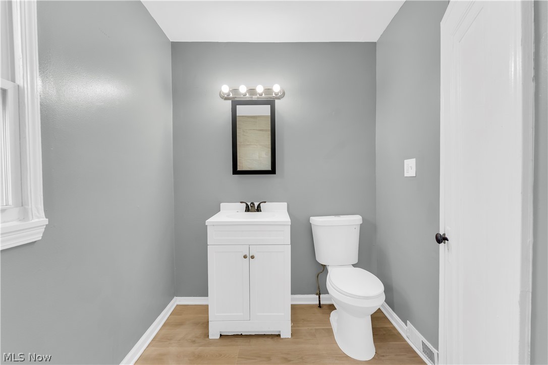 12808 Havana Road Cleveland, OH 44125 - Photo 15 of 19 Bathroom featuring a white single-vanity cabinet with integrated sink, a rectangular framed mirror with overhead vanity lighting, a white toilet, and wood-finish flooring
