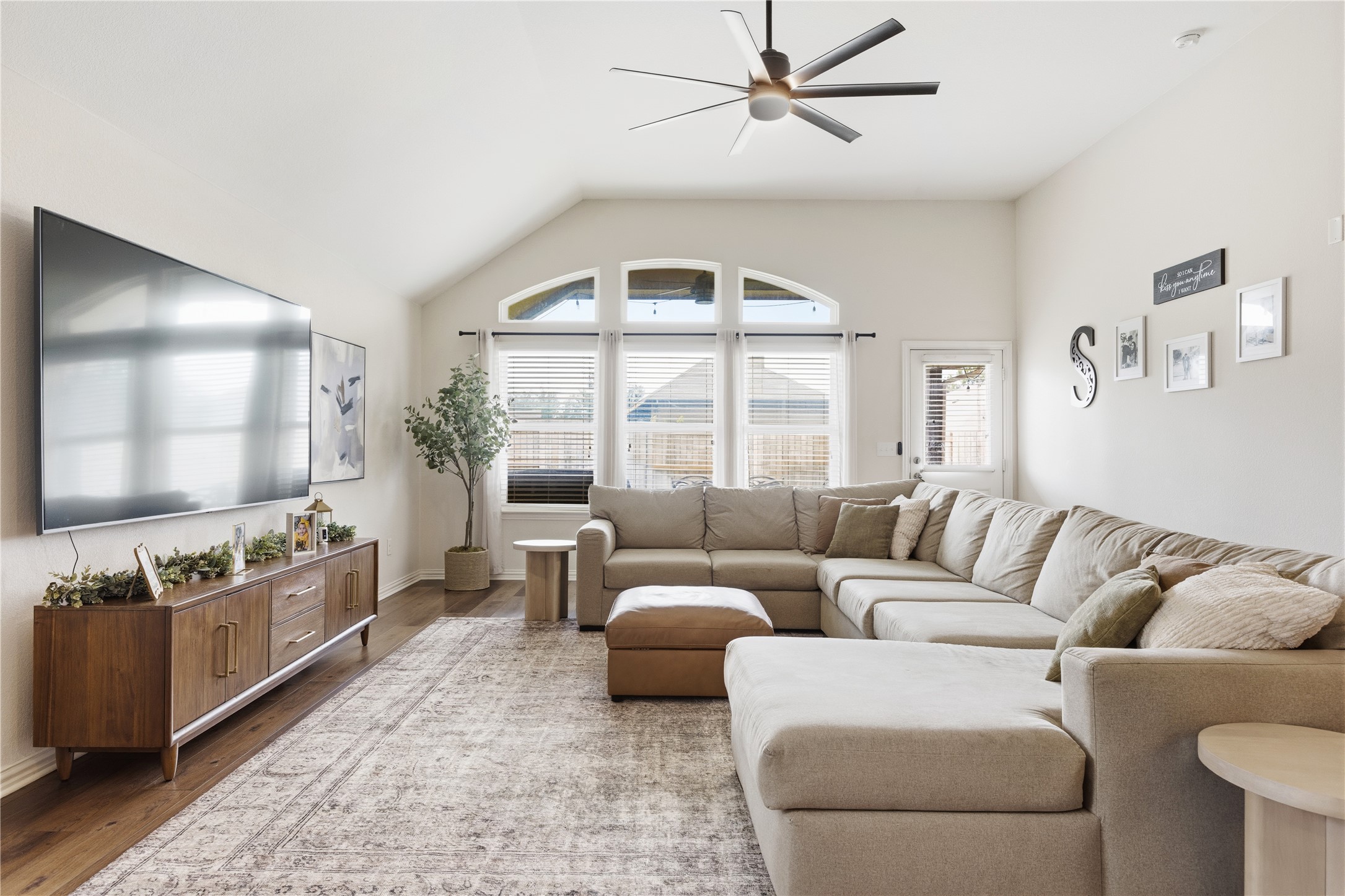 486 Pond View Pass Buda, TX 78610 - Photo 15 of 39 Vaulted ceiling living area featuring wood-finish flooring, a contemporary ceiling fan, and arched window details
