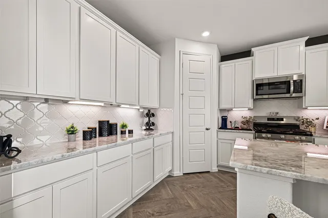 a kitchen with stainless steel appliances granite countertop a stove a sink dishwasher a refrigerator white cabinets and couches with wooden floor