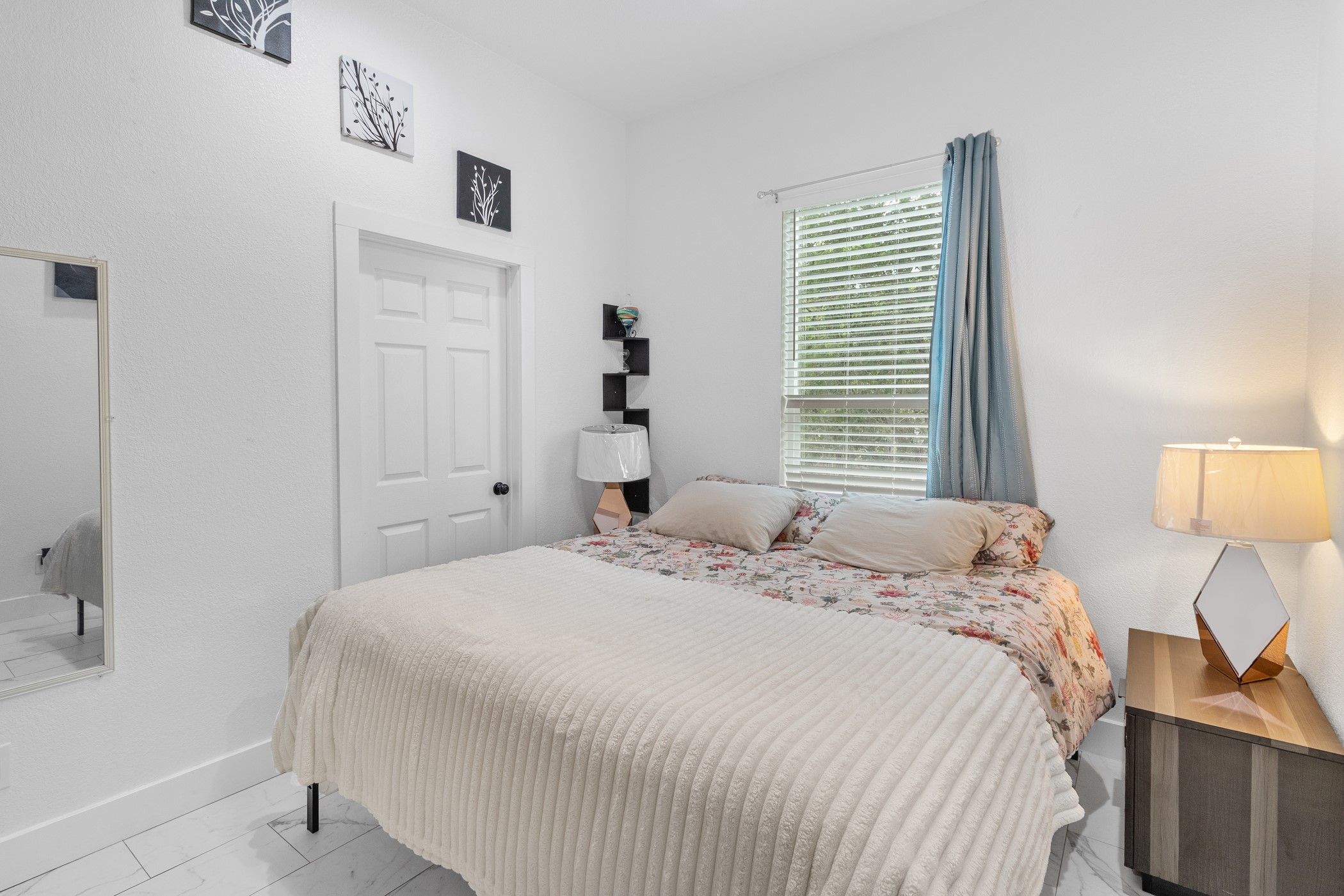 123 Zacate Street Elgin, TX 78621 - Photo 8 of 33 Bright room featuring white walls, a single window with blinds and blue drapery, a paneled door with black hardware, and wood-finish flooring