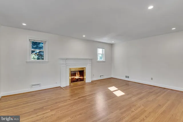 an empty room with wooden floor fireplace and windows