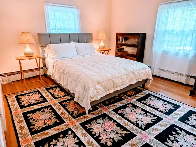 a bed sitting in a bedroom next to a window with a lamp and a table