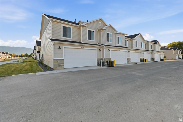 2257 South 1090 West, Unit 74 Nibley, UT 84321 - Photo 3 of 40 Townhome exterior featuring light-colored siding, stone accents, black roofs, and individual garages