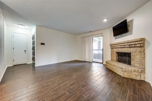 a view of an empty room with wooden floor fireplace and a window