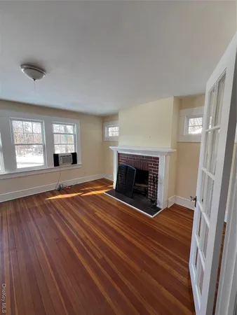 an empty room with wooden floor fireplace and windows