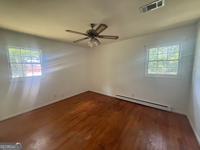 an empty room with wooden floor fan and windows