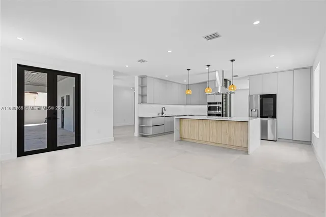 a large white kitchen with stainless steel appliances kitchen island a large counter top and a refrigerator