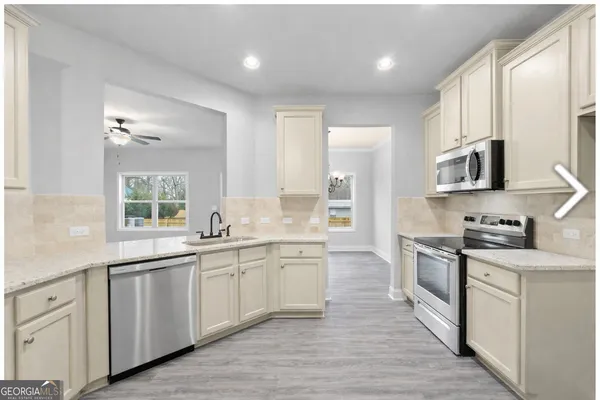 a large kitchen with stainless steel appliances granite countertop a stove top oven a sink dishwasher and white cabinets with wooden floor