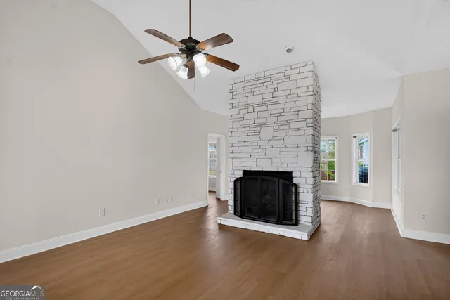 an empty room with wooden floor a fireplace a ceiling fan and a kitchen counter top