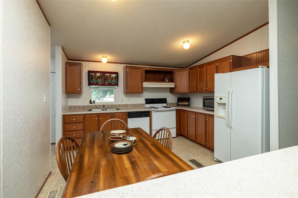207 Lazy B Lane Springtown, TX 76082 - Photo 12 of 39 Kitchen featuring vaulted ceiling, sink, a textured ceiling, light tile patterned flooring, and white appliances