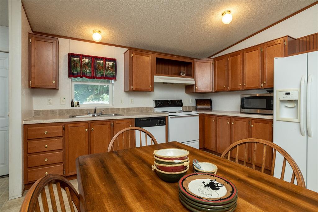 207 Lazy B Lane Springtown, TX 76082 - Photo 16 of 39 Kitchen with a textured ceiling, white appliances, vaulted ceiling, and sink