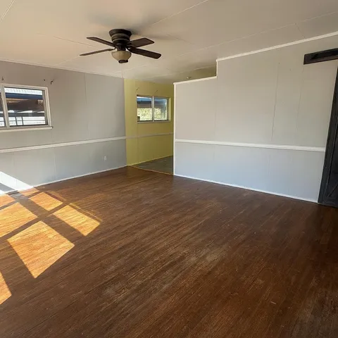 an empty room with wooden floor chandelier fan and windows