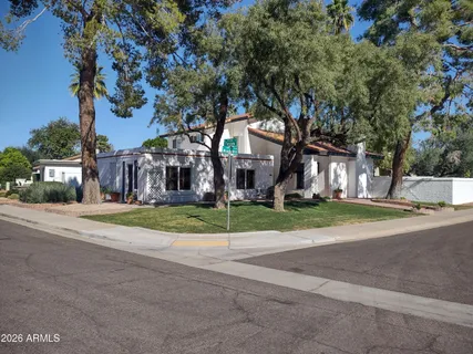 a tree in front of a brick house with a big yard and large trees