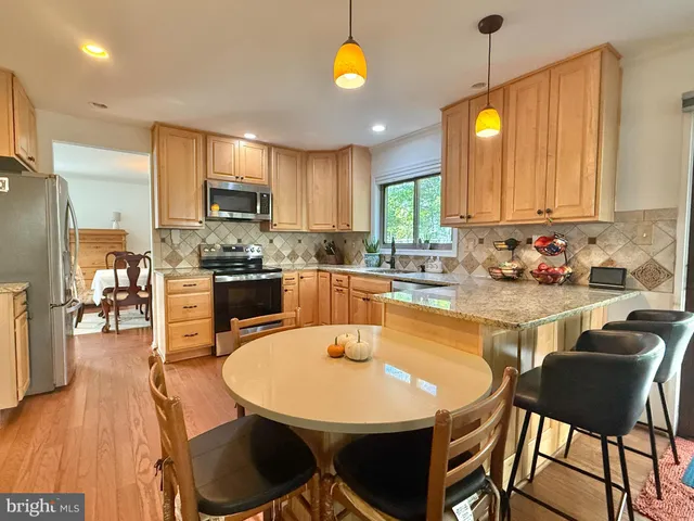 a kitchen with stainless steel appliances kitchen island granite countertop a sink a stove a dining table and chairs with wooden floor