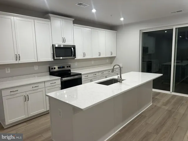 a kitchen with stainless steel appliances a sink dishwasher a stove top oven a refrigerator with white cabinets and wooden floor