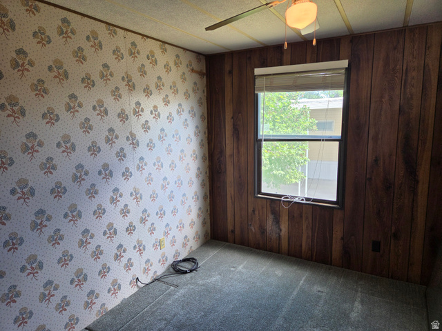 1111 North 2000 West, Unit 147 Ogden, UT 84404 - Photo 10 of 12 Room featuring a window with blinds, wood-paneled wall, patterned wallpaper, and ceiling fan with light fixture