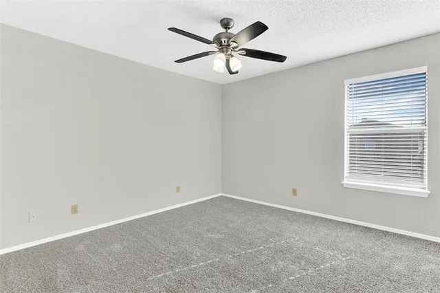 an empty room with chandelier fan and windows
