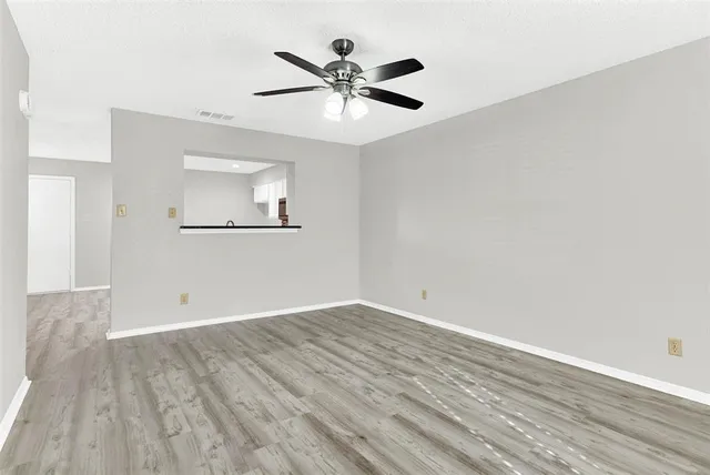an empty room with wooden floor ceiling fan and windows