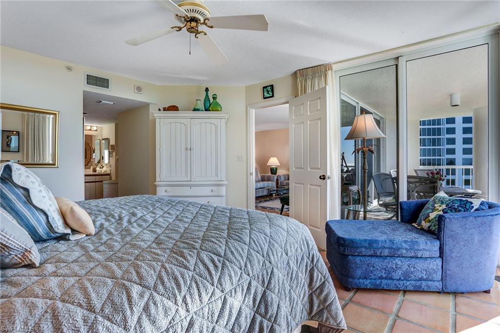 50 Seagate Drive, Unit 402B Naples, FL 34103 - Photo 12 of 26 a spacious bedroom with a bed a chandelier and couch