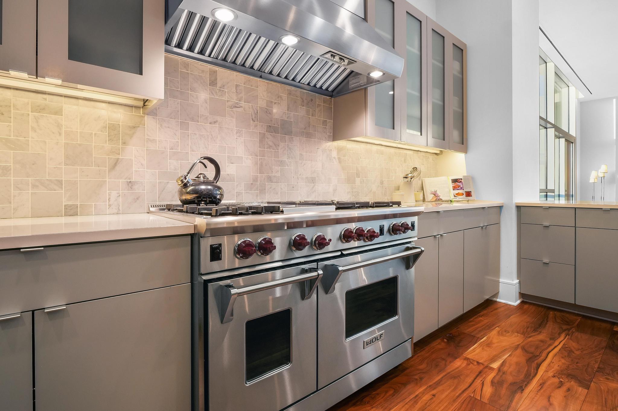 555 East 5th Street, Unit 3022 Austin, TX 78701 - Photo 12 of 40 Kitchen featuring gray cabinets, range with two ovens, wall chimney exhaust hood, glass insert cabinets, and dark wood-style floors